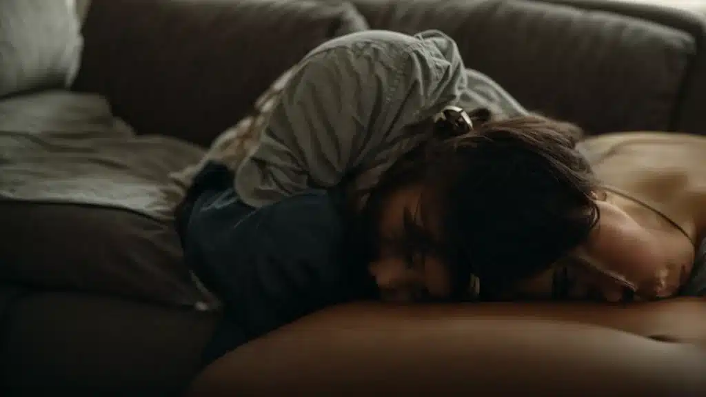 a person sits curled up on a couch, clutching their head in distress.