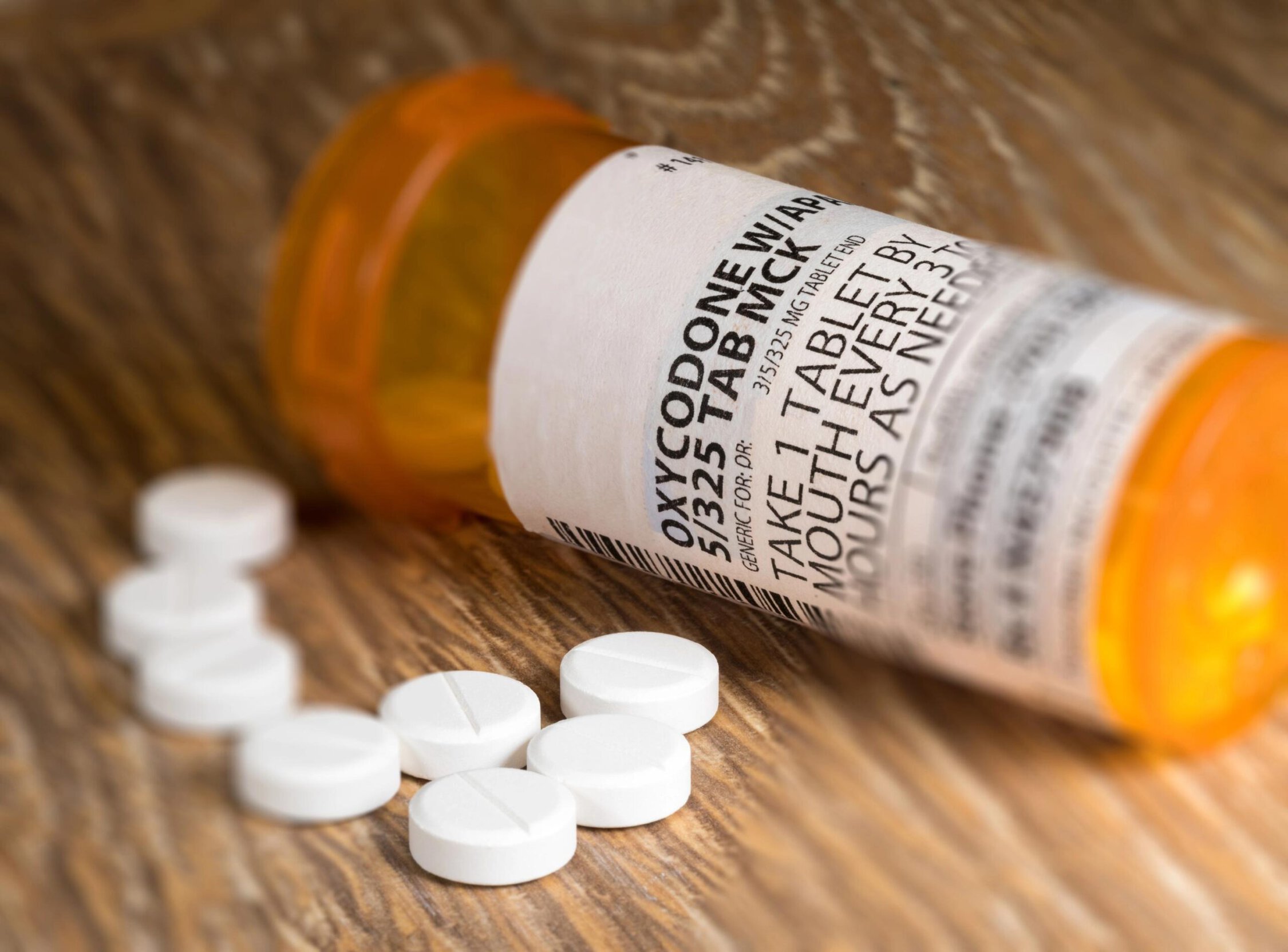 Oxycodone medication bottle with white pills on wooden surface.