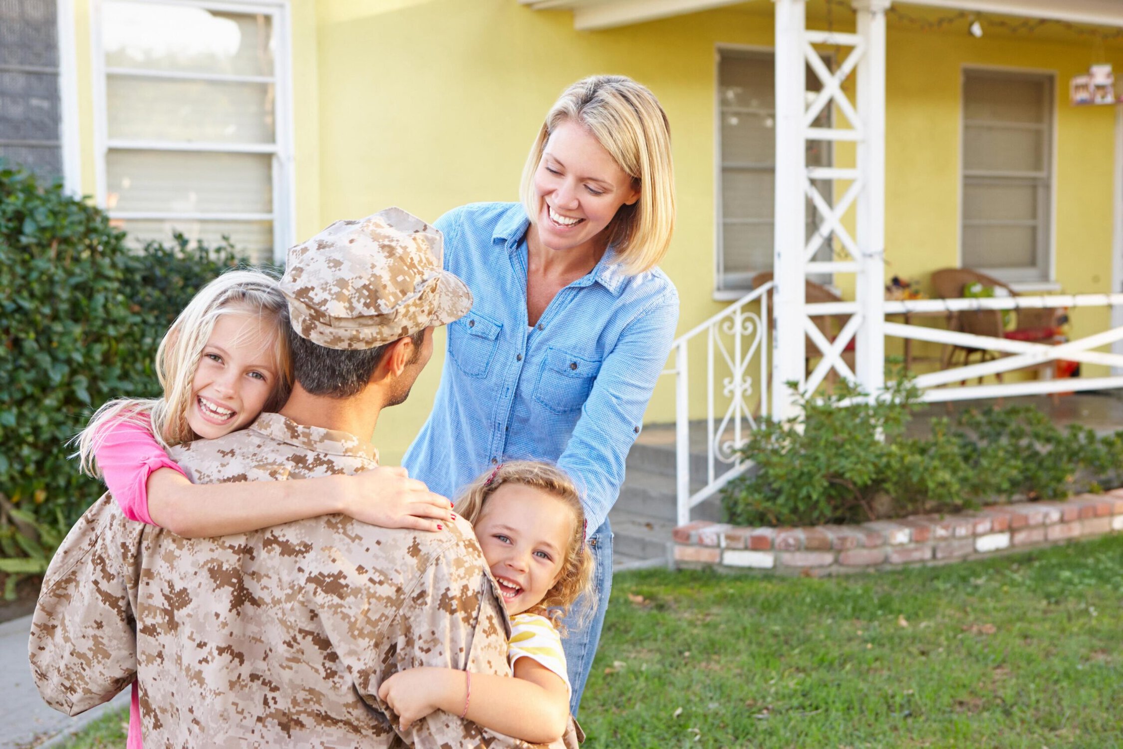 Happy family reunion with soldier in uniform outside a yellow house.