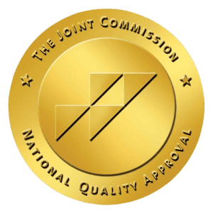 A gold seal with the text "The Joint Commission" and "National Quality Approval" surrounding a styli.