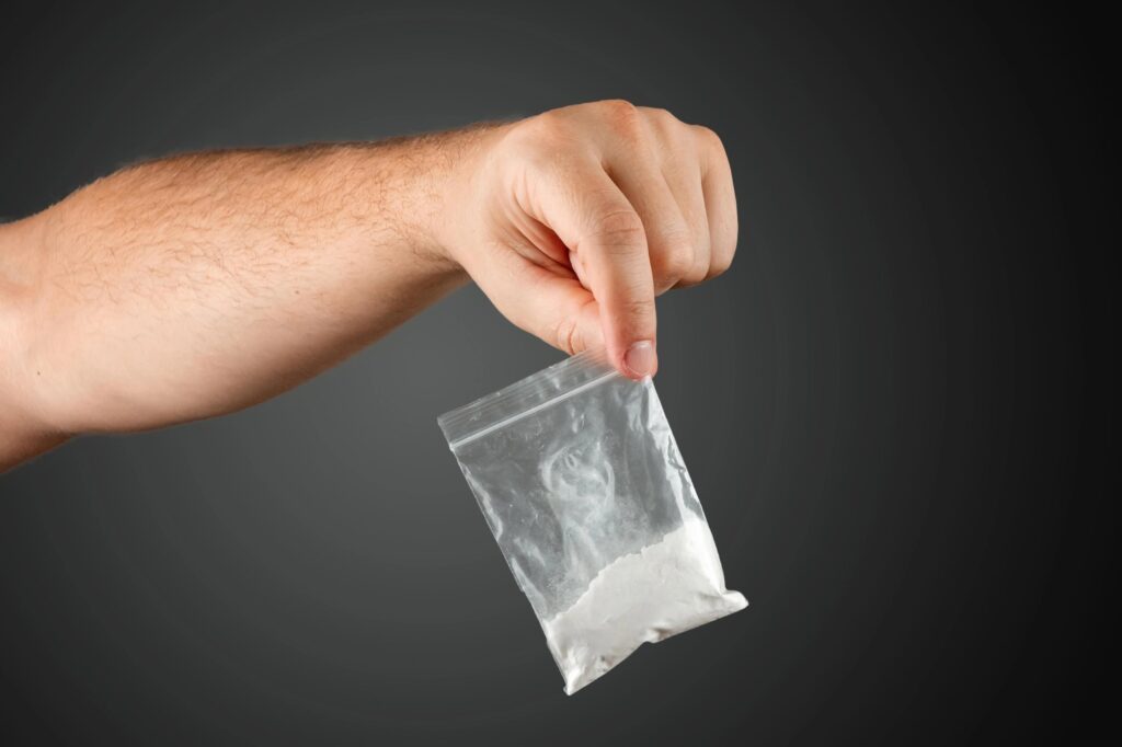 Hand holding a small plastic bag with white powder against dark background.