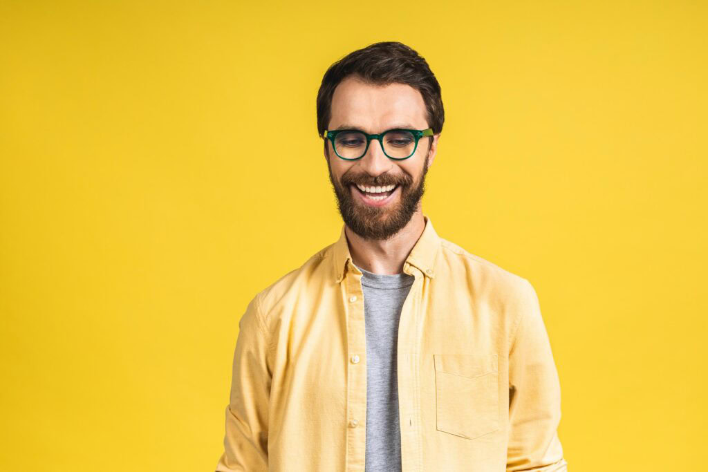 Smiling man with glasses against yellow background for drug rehab promotion.