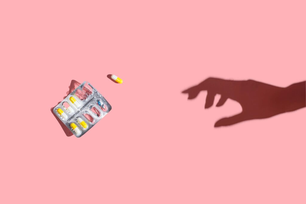 Hand reaching for pills and medication on pink background.