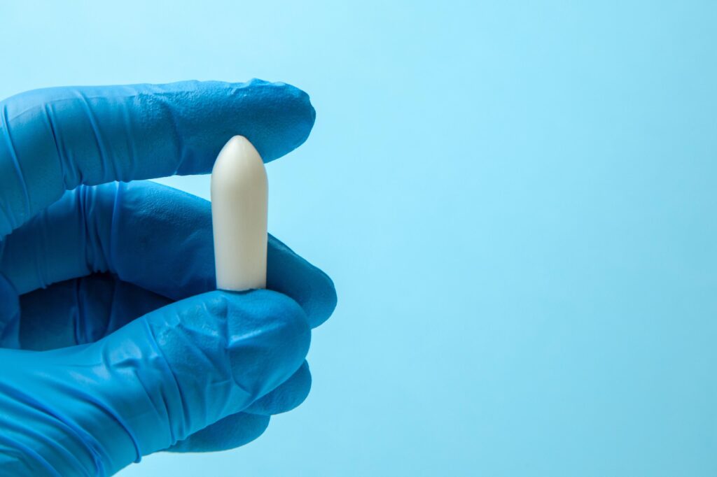 Close-up of a hand in a blue glove holding a white pill against a light blue background.