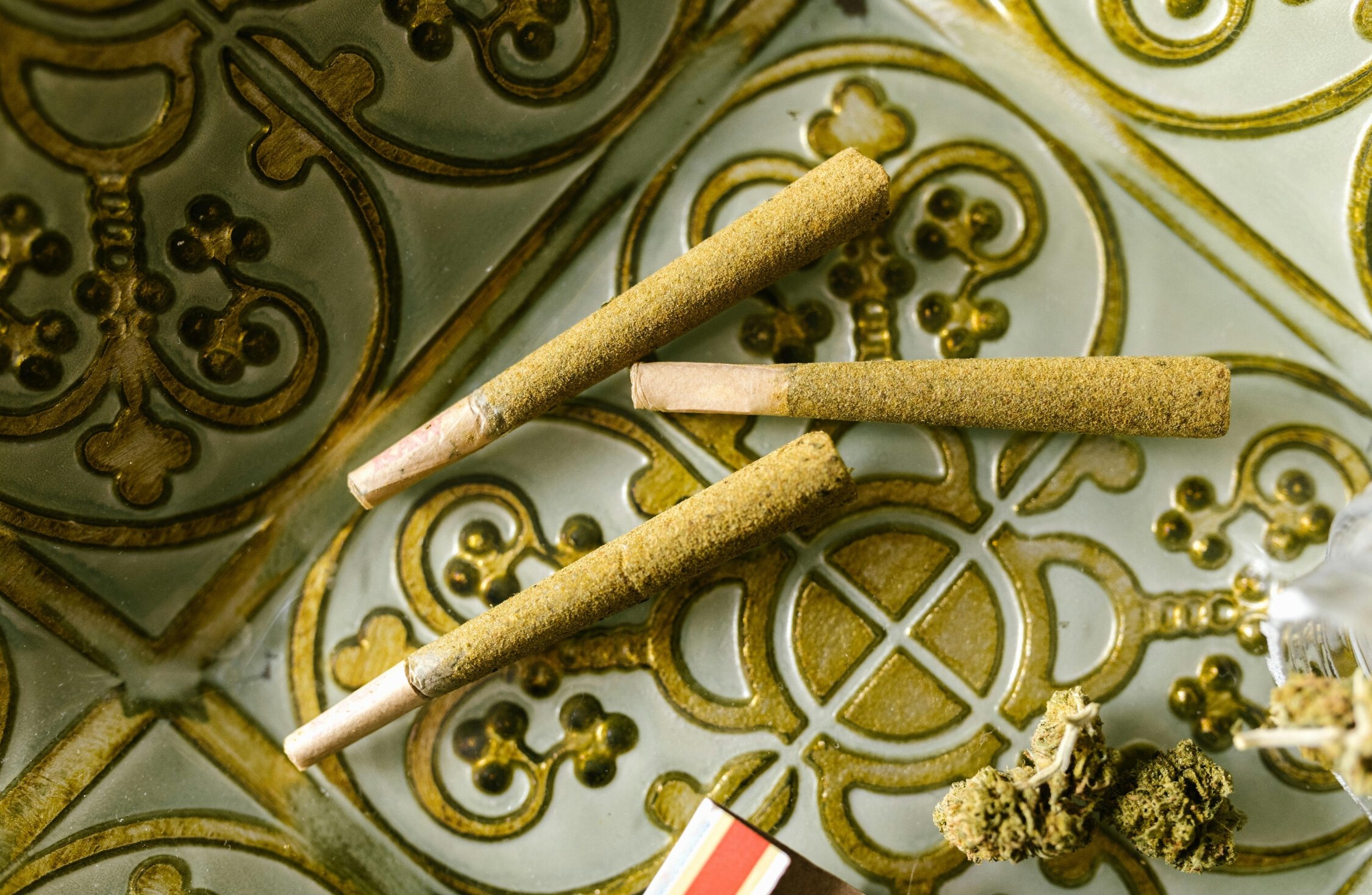 Marijuana joints and cannabis buds on decorative surface.